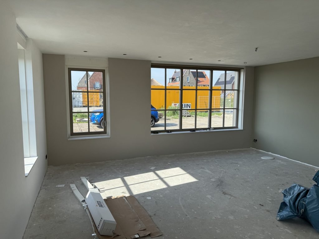 Nieuwbouwkamer met warm grijze wanden en grote ramen, vloer nog in de bouwstaat