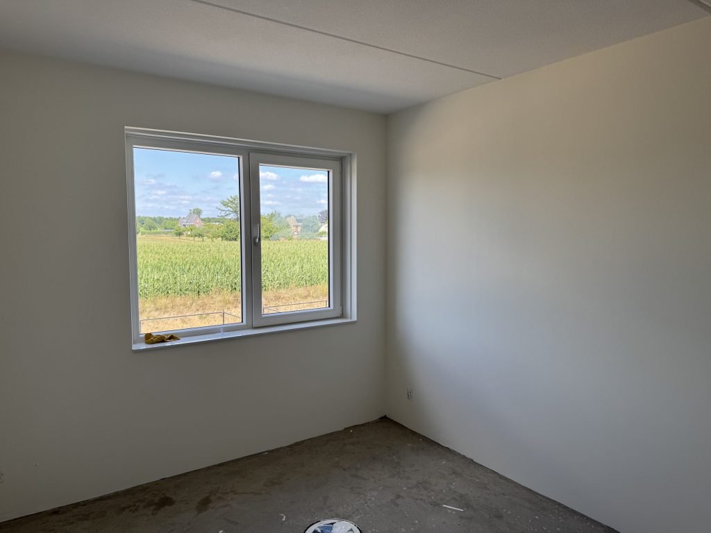 Lichte nieuwbouwkamer met strak afgewerkte witte wanden en een raam met uitzicht over het land
