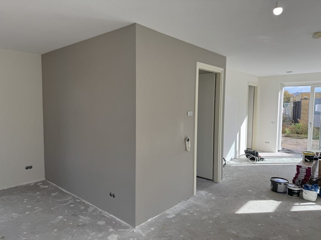 Grijs gesausde wand in een nieuwbouwwoning met verfemmers en gereedschap op de vloer