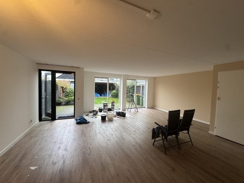Lege woonkamer met lichte, egaal gesausde wanden, een houten vloer en openslaande tuindeuren