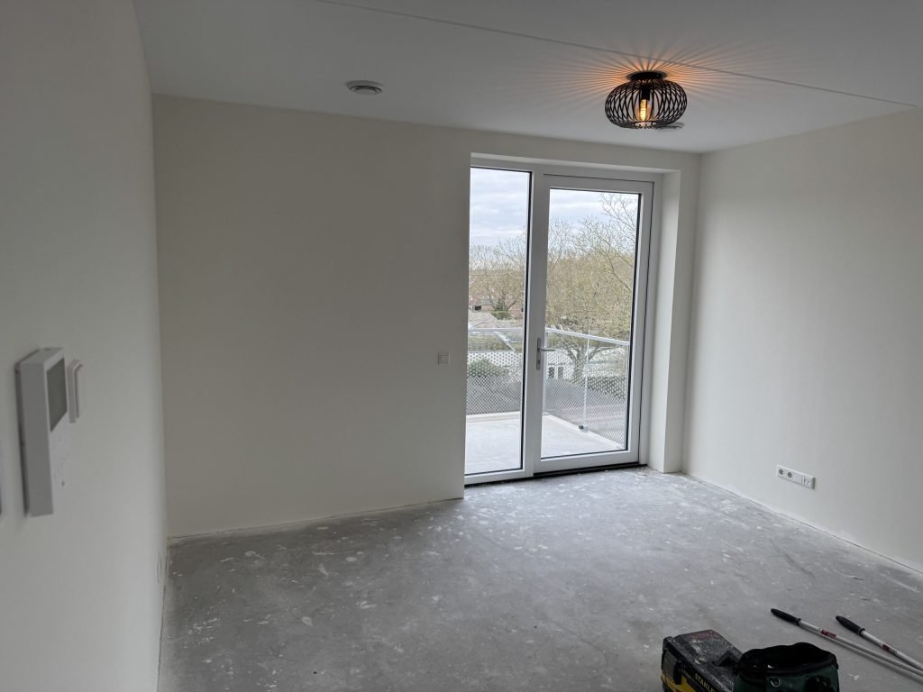 Nieuwbouwkamer met witte wanden en een glazen balkondeur, klaar voor oplevering